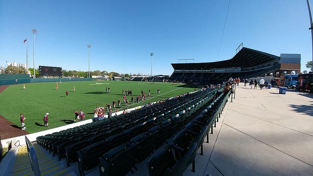 View from the left-field concourse at UFCU Disch–Falk Field — pre-game warm-ups, scoreboard in left, fans filtering in. Photo: Ensign beedrill / Wikimedia Commons (CC BY-SA 4.0)