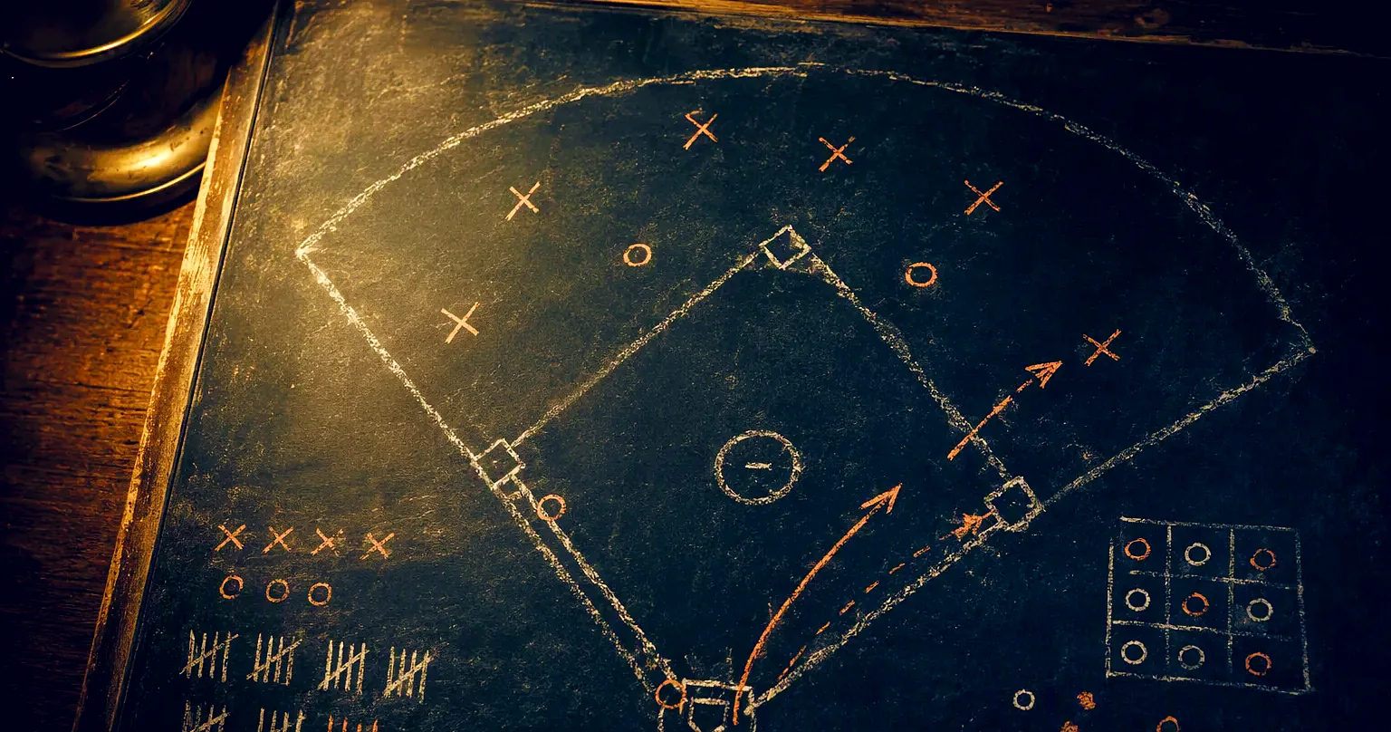 A manager's chalkboard: a baseball diamond drawn in white chalk with fielders marked, a runner's path from first to third arrowed in orange, tally marks and a strike-zone grid in the corners.